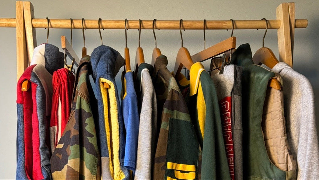 Clothing rack with various jackets and hoodies hanging on it against a neutral wall.